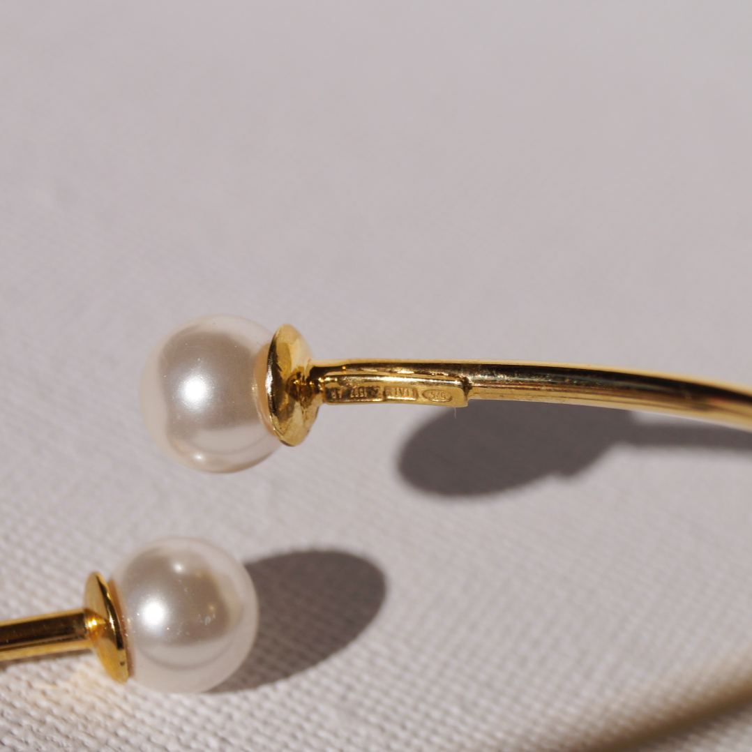 Potvrda autenticnosti.
Zlatna kruta narukvica s dva prirodna bisera na krajevima, prikazana na svijetloj podlozi.