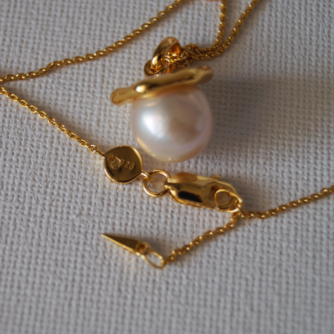 Pozlaćeni srebrni lancic s prirodnim bisernim privjeskom i uklonjivim zlatnim prstenom, fotografirano na neutralnoj podlozi.